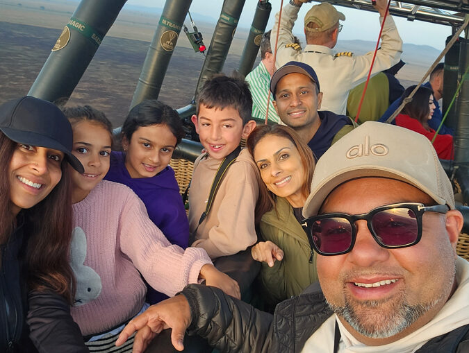 A woman in a natural rock pool at the top of a waterfall, with a rainbow in the spray.